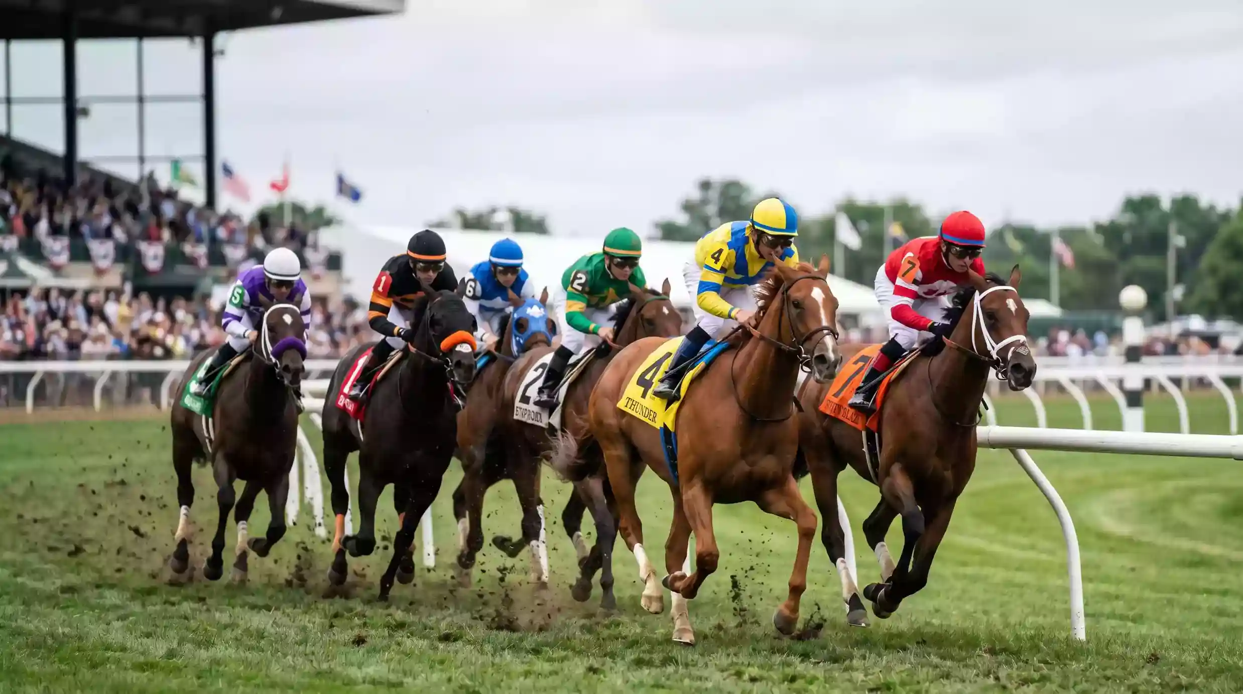 Racehorses competing at a UK flat meeting with packed grandstands in the background